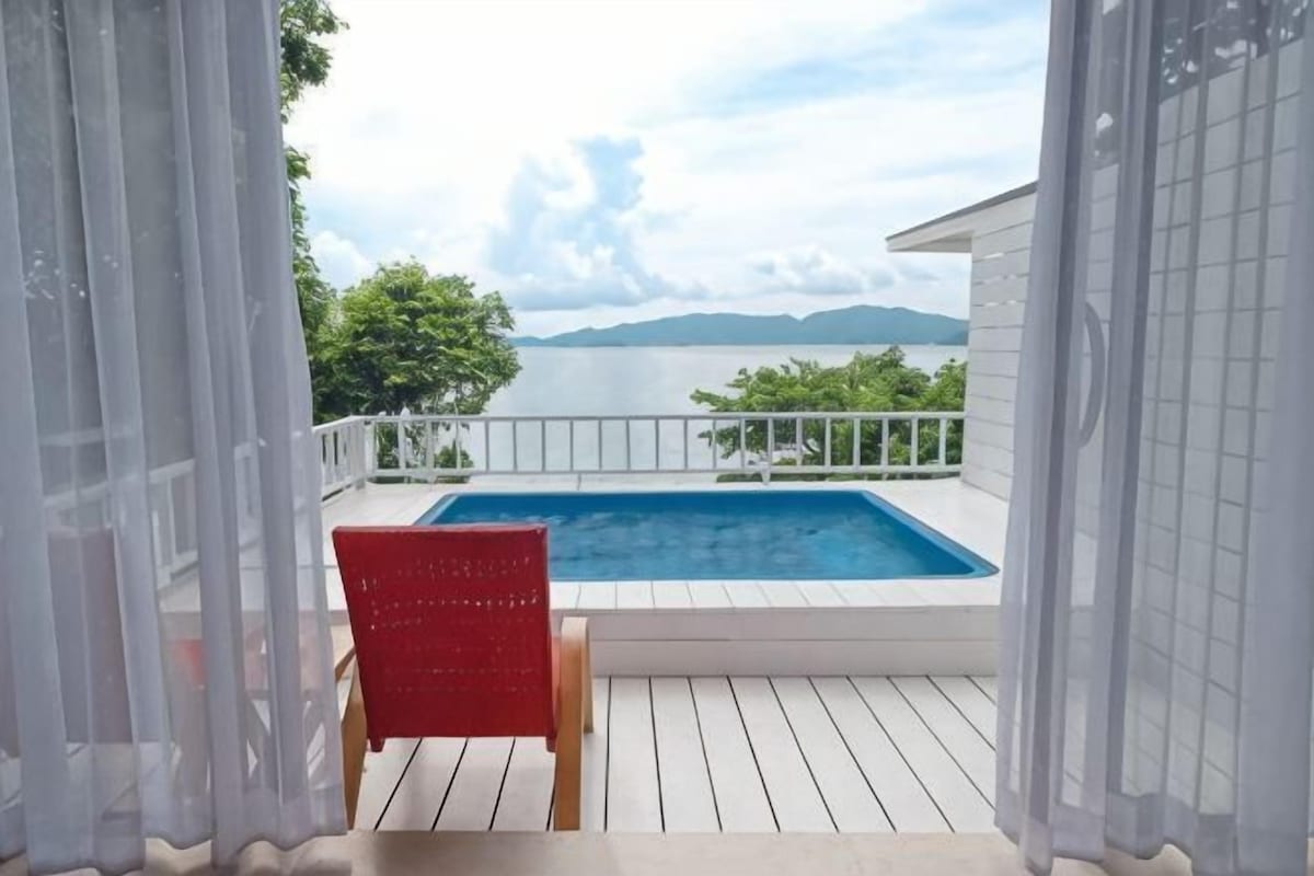A pool on a deck with a view of the sea and mountains.
