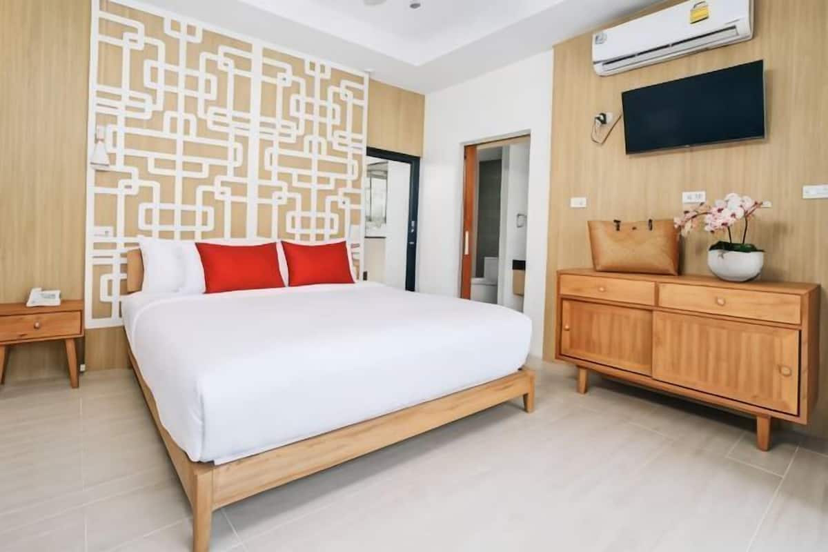 A bedroom with a bed, wooden nightstand, dresser, and a wall-mounted TV.