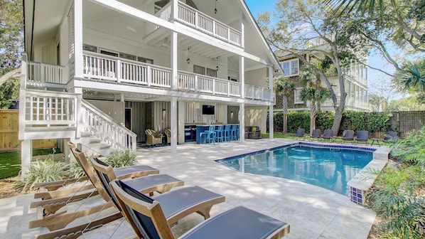 A two-story house with a balcony, a pool, and outdoor seating.