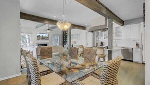Une cuisine moderne avec des meubles blancs, un îlot central et un coin repas comprenant une table en verre et des chaises en osier.