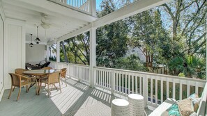 A covered outdoor area with a dining table and chairs, a ceiling fan, and a view of trees and greenery.