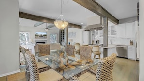 A modern kitchen with white cabinetry, a glass dining table, and woven chairs.