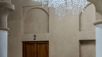 Una habitación con una puerta de madera marcada con el número 2, un banco blanco y una lámpara colgante.