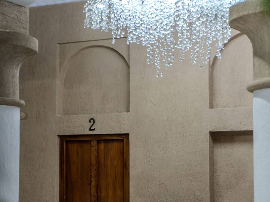 Una habitación con una puerta de madera marcada con el número 2, un banco blanco y una lámpara colgante.