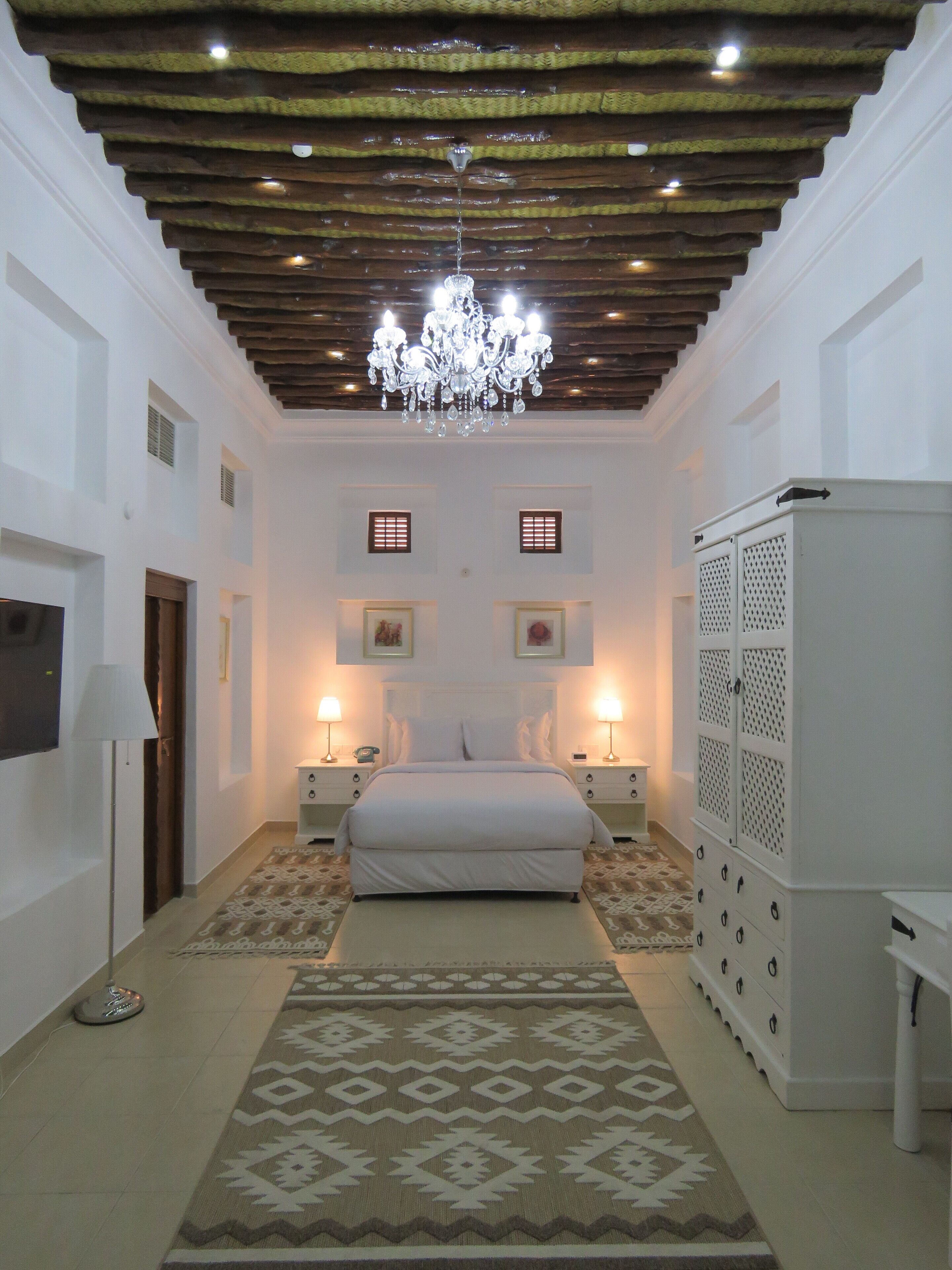 A bedroom with a bed centered between two nightstands, a chandelier, and a wardrobe with a lattice design.