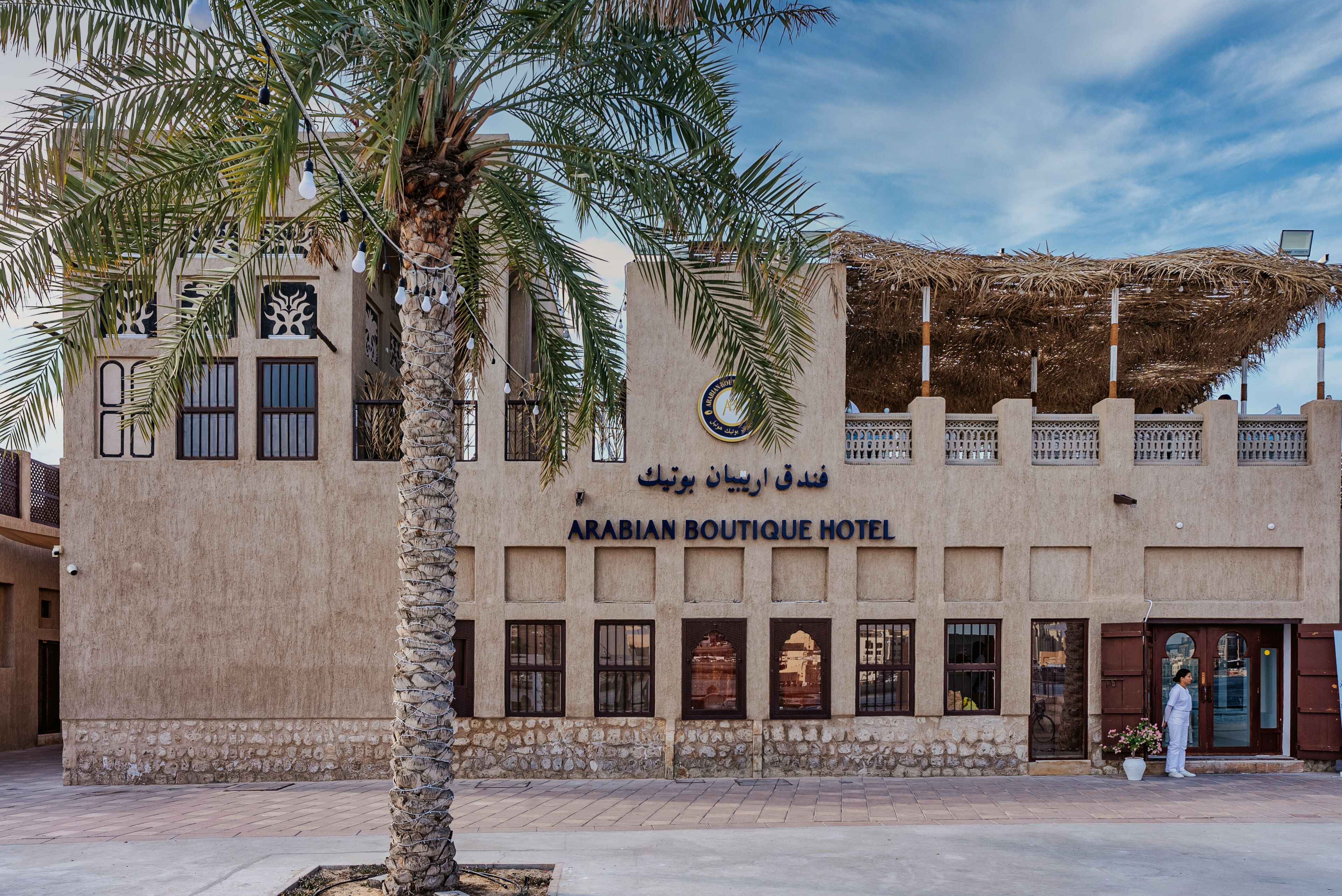 The exterior of the Arabian Boutique Hotel with a palm tree in the foreground and a clear sky.