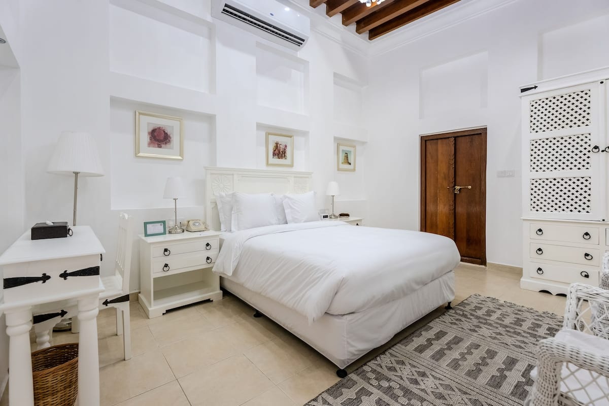 Un dormitorio con una cama grande, mesitas de noche blancas, un aparador y una alfombra estampada.
