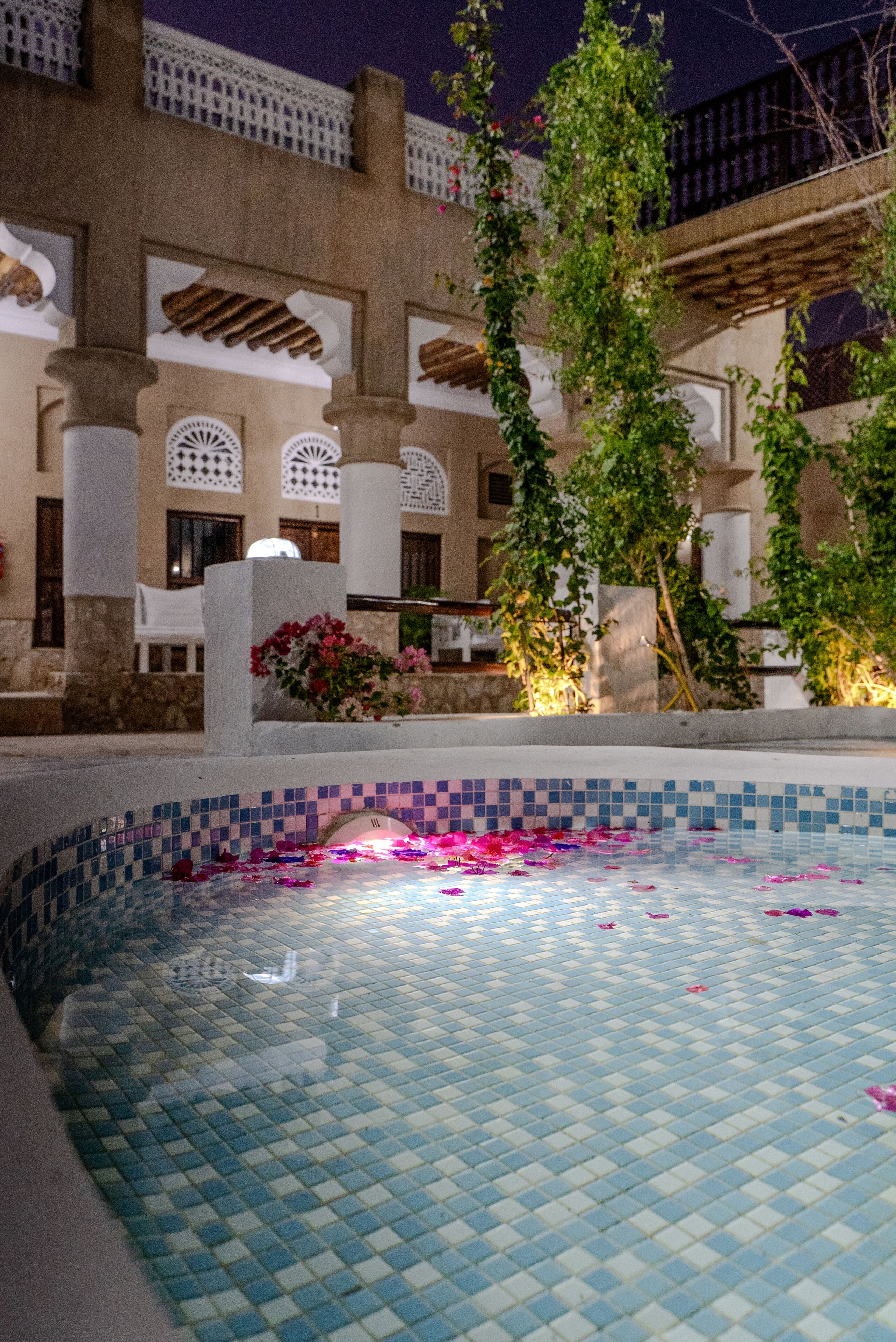 Una piscina con piastrelle blu e bianche, circondata da un edificio con archi e colonne.
