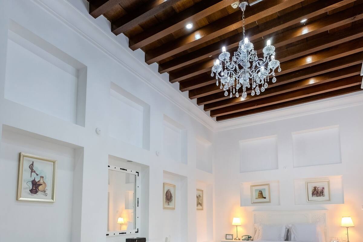 Un dormitorio con cama, mesitas de noche, escritorio, silla, lámpara de araña y alfombra estampada.