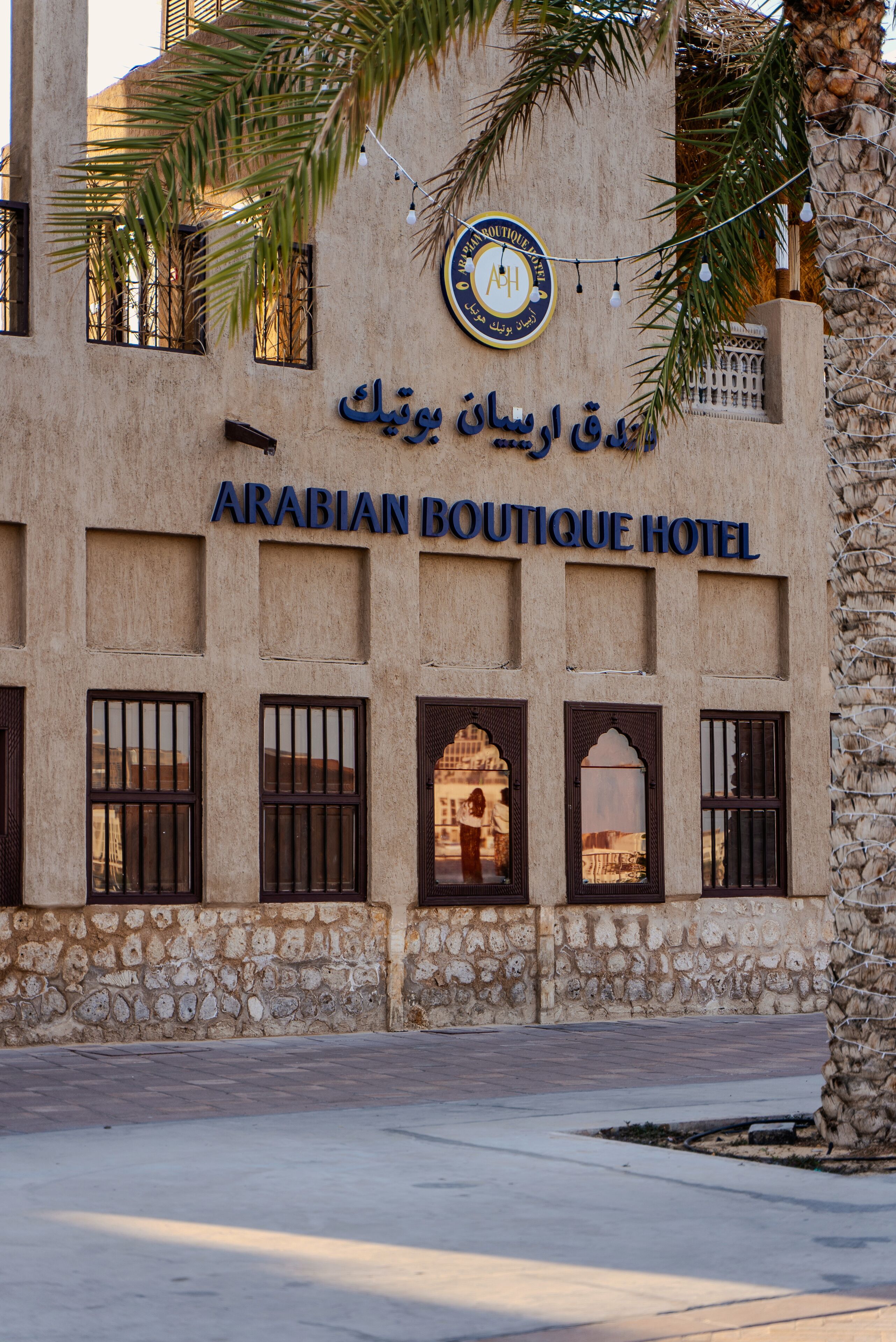 The exterior of the Arabian Boutique Hotel with stone walls, arched windows, and a palm tree.