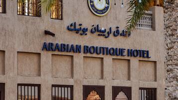 The exterior of the Arabian Boutique Hotel with stone walls, arched windows, and a palm tree.