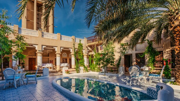 Um pátio com piscina, área de estar ao ar livre e um edifício com arcos e colunas.