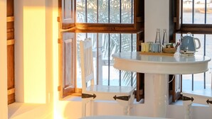 Quarto com uma cama grande, uma mesinha de cabeceira com chaleira e uma janela com vista para palmeiras.