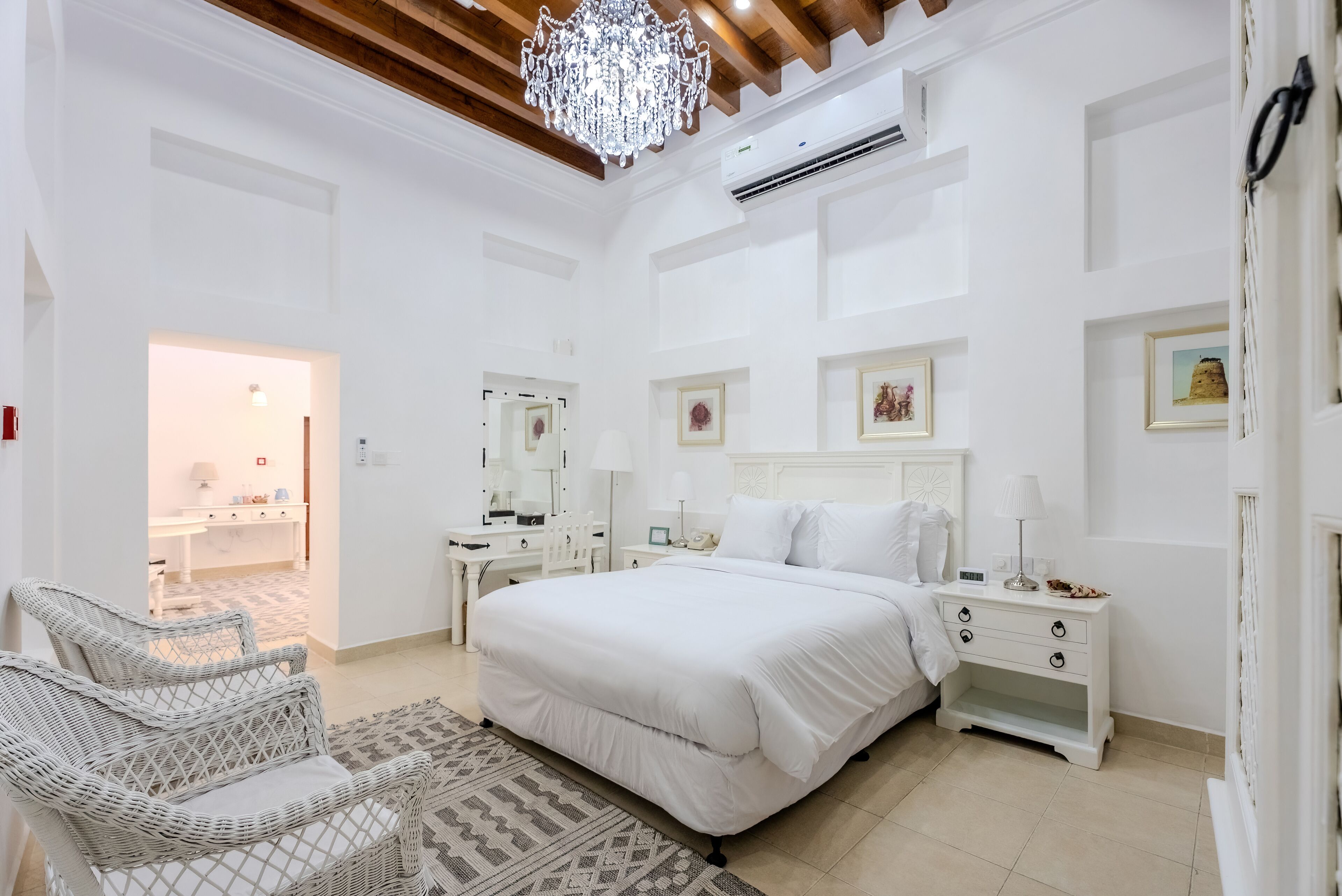 A bedroom with a large bed, a nightstand, a dresser, a chair, and a chandelier.