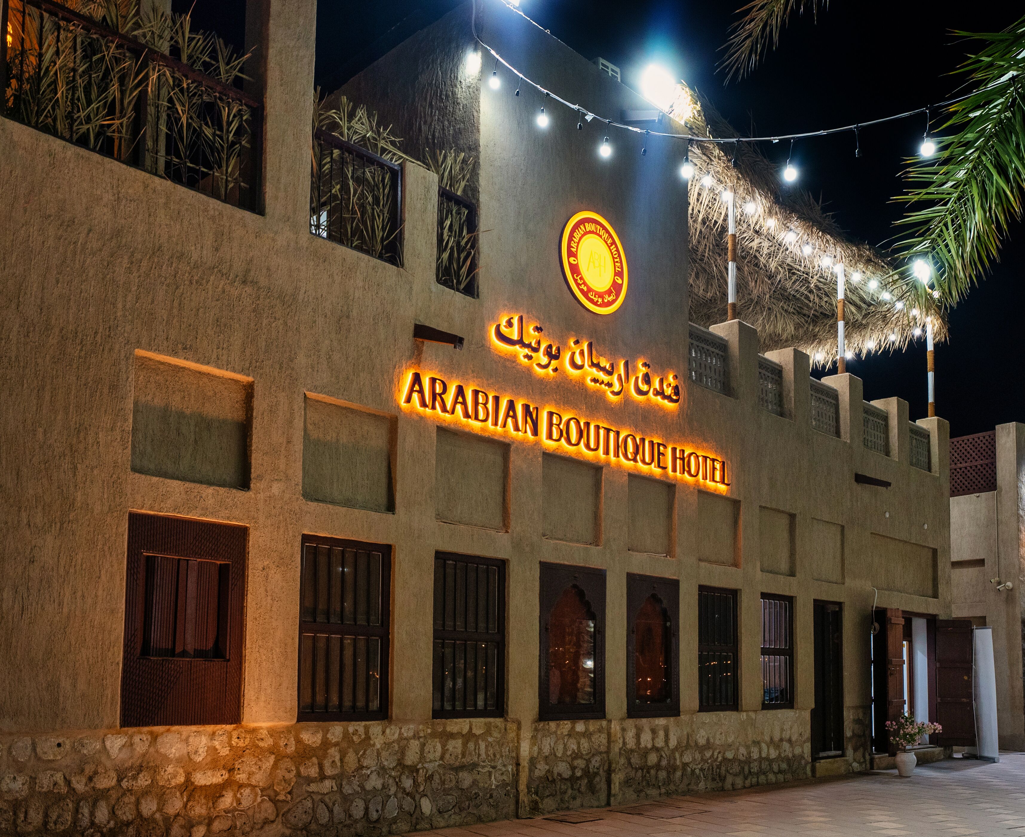 L’extérieur de l’hôtel Arabian Boutique présente une enseigne en arabe et en anglais, des murs en pierre et un palmier.