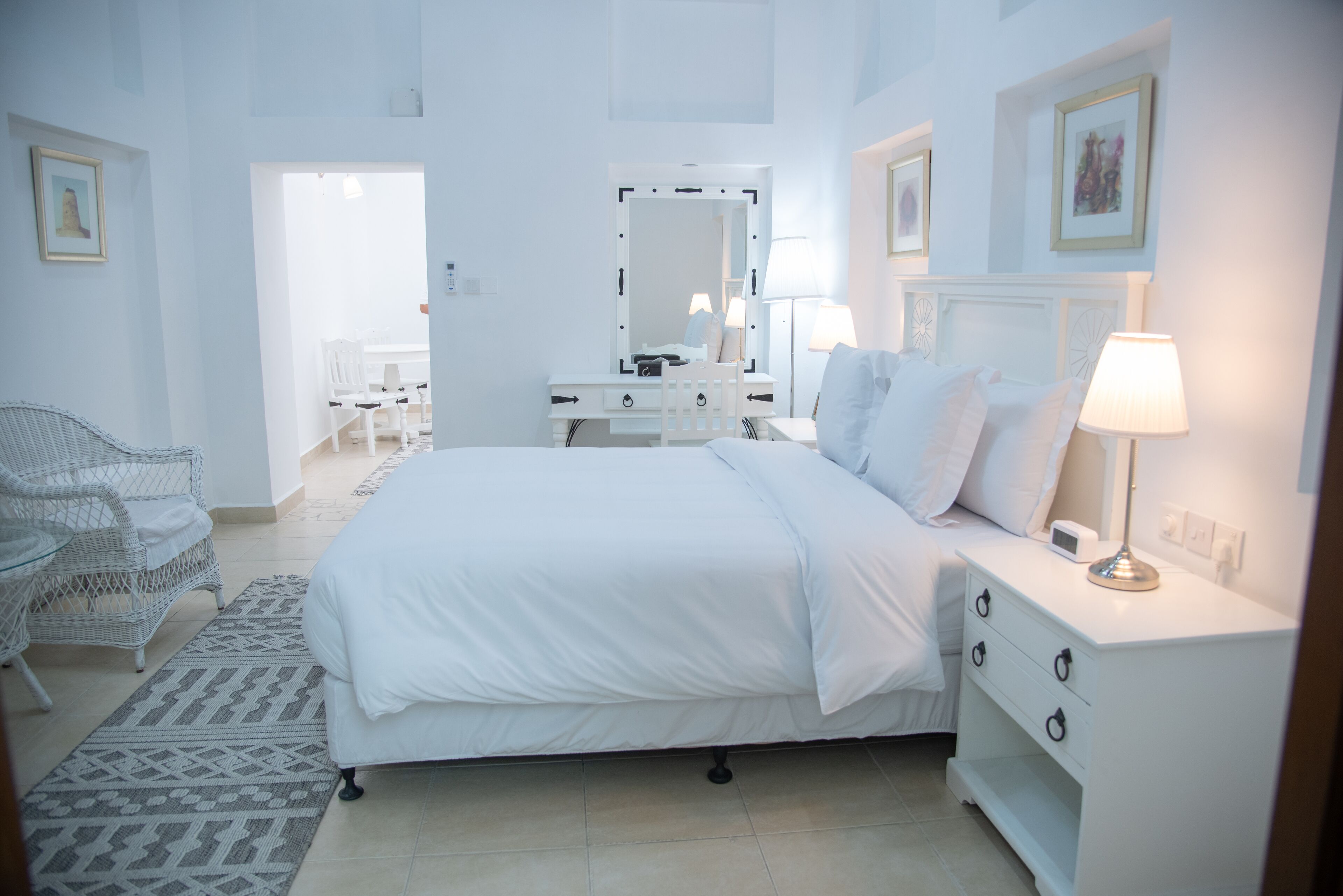A white-themed bedroom with a bed, bedside table, lamp, and a chair.