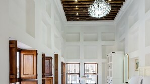 Une pièce spacieuse avec un grand lit, une chaise en osier blanche, une armoire en bois et un lustre.