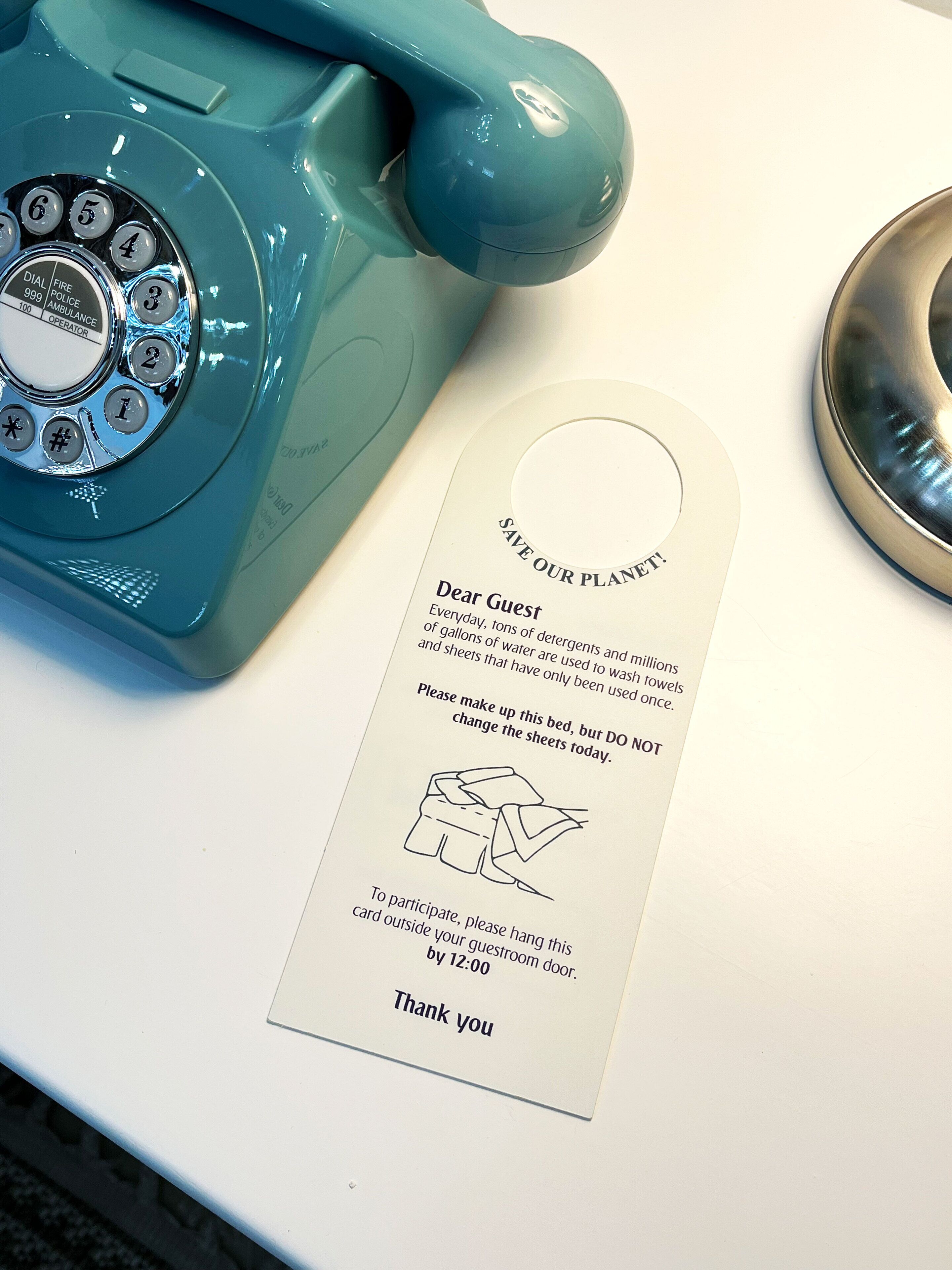 Un teléfono giratorio color turquesa y un cartel solicitando a los huéspedes que cambien las sábanas.