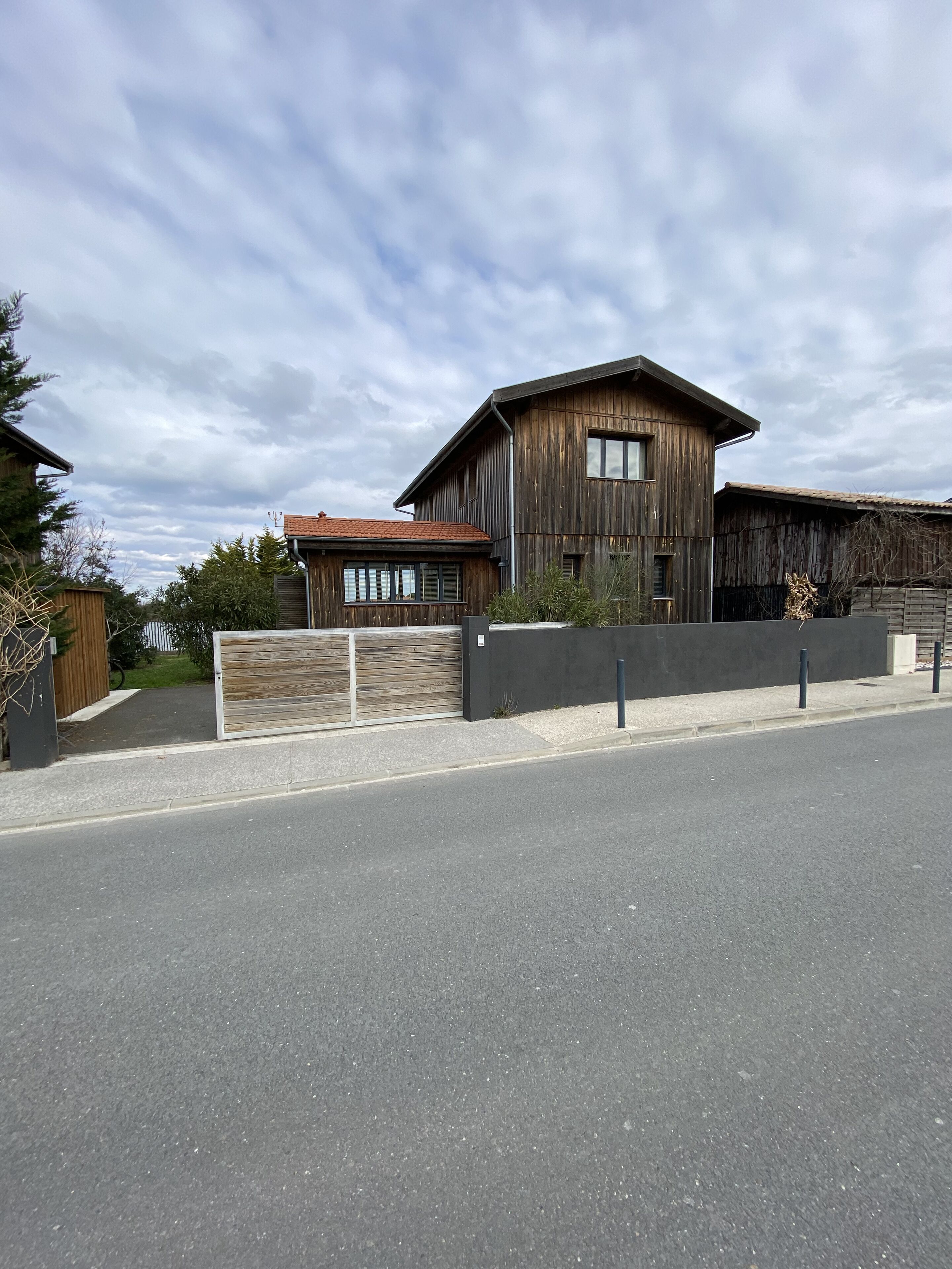 A two-story wooden house with a garage, a gated driveway, and a clear sky.