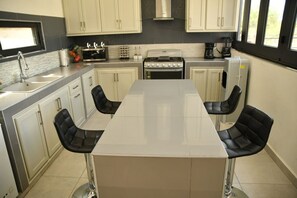 Una cocina moderna con una isla central, dos sillas negras y un lavamanos de acero inoxidable.