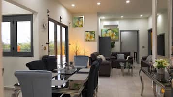 A modern living room with a dining area, large windows, and artwork on the walls.