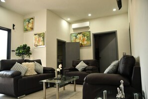 Ein modernes Wohnzimmer mit drei dunkelbraunen Ledersofas, einem Glastisch und floralen Gemälden an den Wänden.