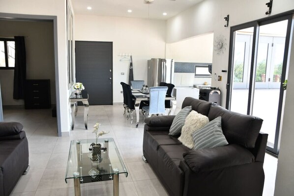 A modern living room with a glass coffee table, a dark leather sofa, and a dining area with a table and chairs.