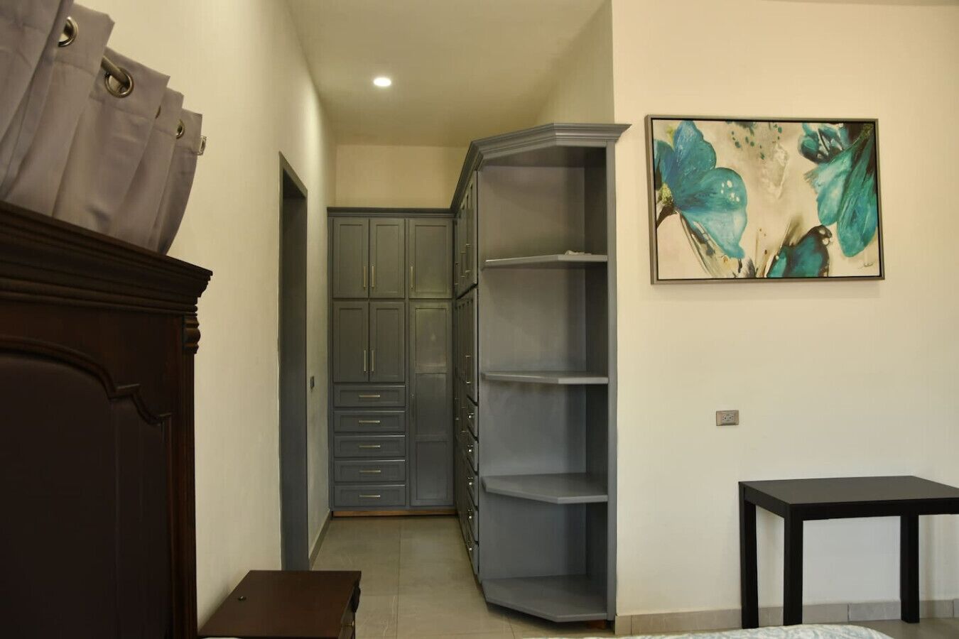 A room with a wardrobe, a painting, and a small table.
