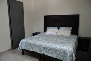Een slaapkamer met een bed, twee nachtkastjes, een donker hoofdeinde en een deur.