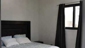 Un dormitorio con cama, ventilador de techo, ventana con cortinas y mesita de noche.