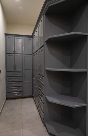 A corner closet with multiple drawers and shelves, a tiled floor, and a plain wall.