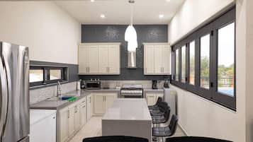 A modern kitchen with a central island, white cabinets, a stainless steel refrigerator, and a large window providing a view of the outdoors.
