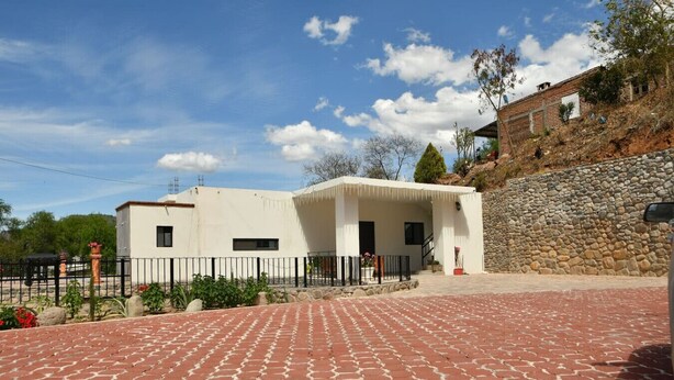 Un edificio de dos pisos con fachada blanca, una pared de piedra a la derecha y un camino de entrada pavimentado.