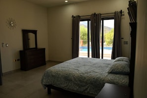 Une chambre avec un lit, une commode, un miroir et une vue sur une piscine, visible à travers une porte-fenêtre coulissante.
