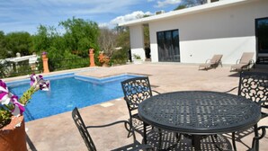 Una piscina con zona de patio, mobiliario exterior y un edificio moderno al fondo.