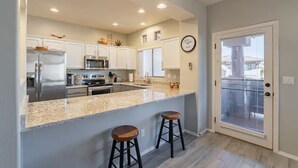 A modern kitchen with white cabinets, stainless steel appliances, a large island with stools, and a sliding glass door leading to a balcony. - Perfect for long-term stay, heated Pool, Spa, Gym  (Oro Valley)