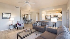 A modern living room with a sofa, coffee table, and lamp, leading to a kitchen area with cabinets and appliances. - Perfect for long-term stay, heated Pool, Spa, Gym  (Oro Valley)