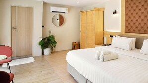 Habitación de hotel con cama, mesita de noche, armario y un espejo. También hay una planta en maceta.