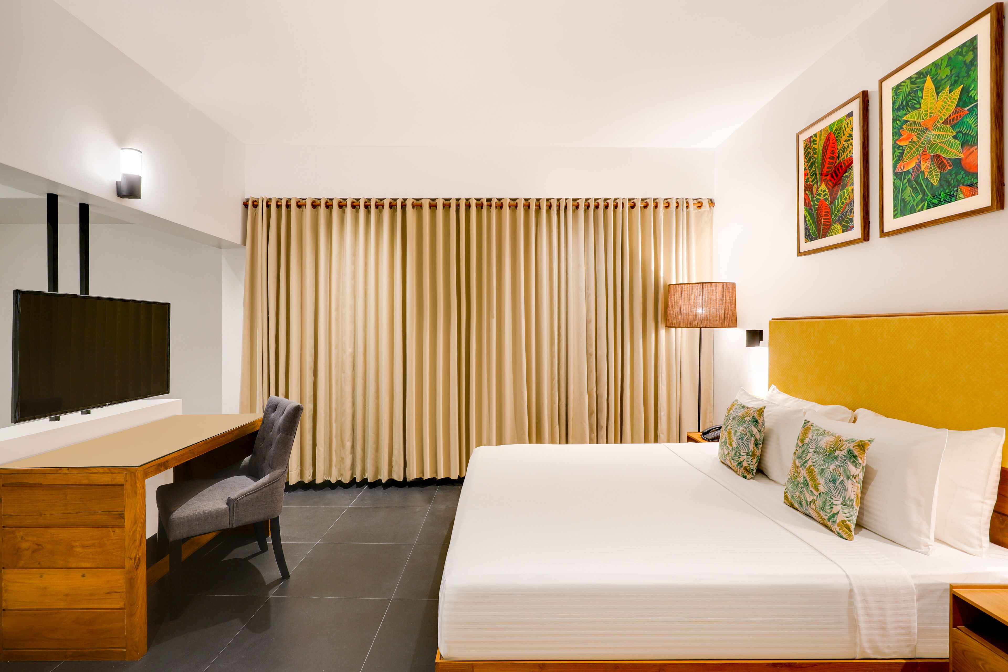 A hotel room with a bed, a desk, a chair, a TV, and curtains.