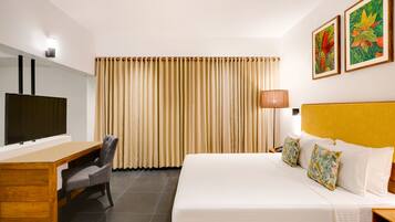A hotel room with a bed, a desk, a chair, a TV, and curtains.