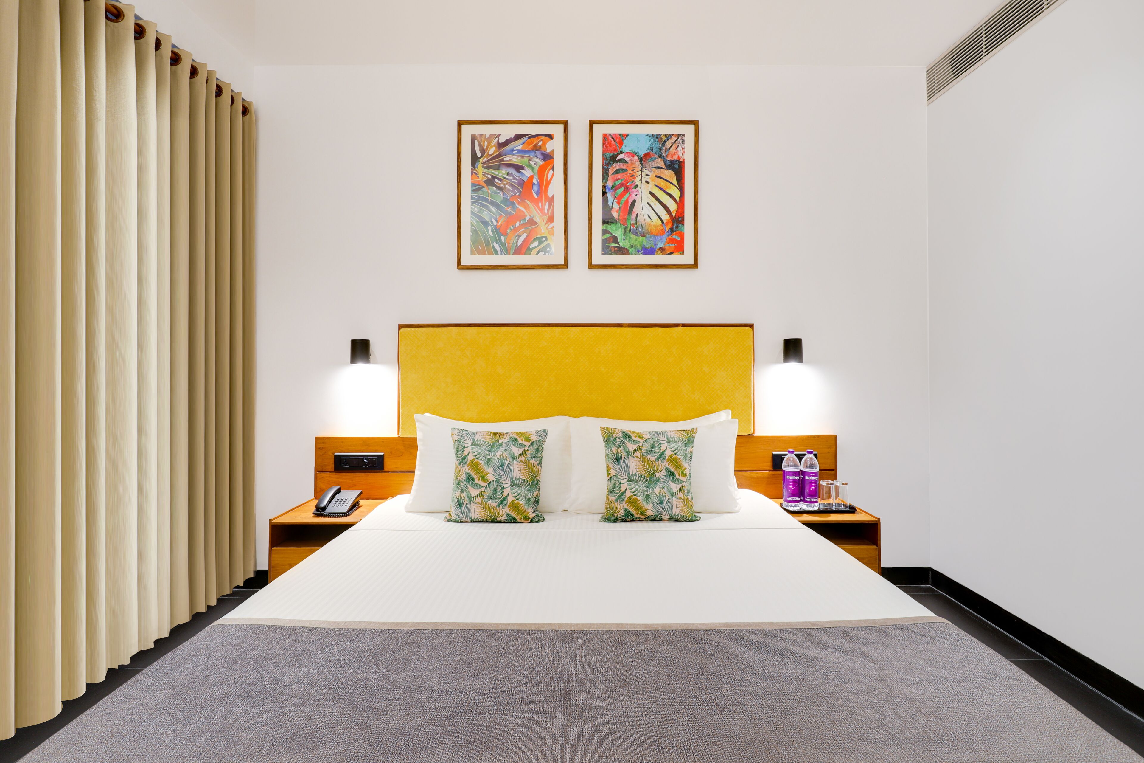 Een hotelkamer met een groot bed, twee wandlampen, een telefoon en twee ingelijste kunstwerken boven het bed.