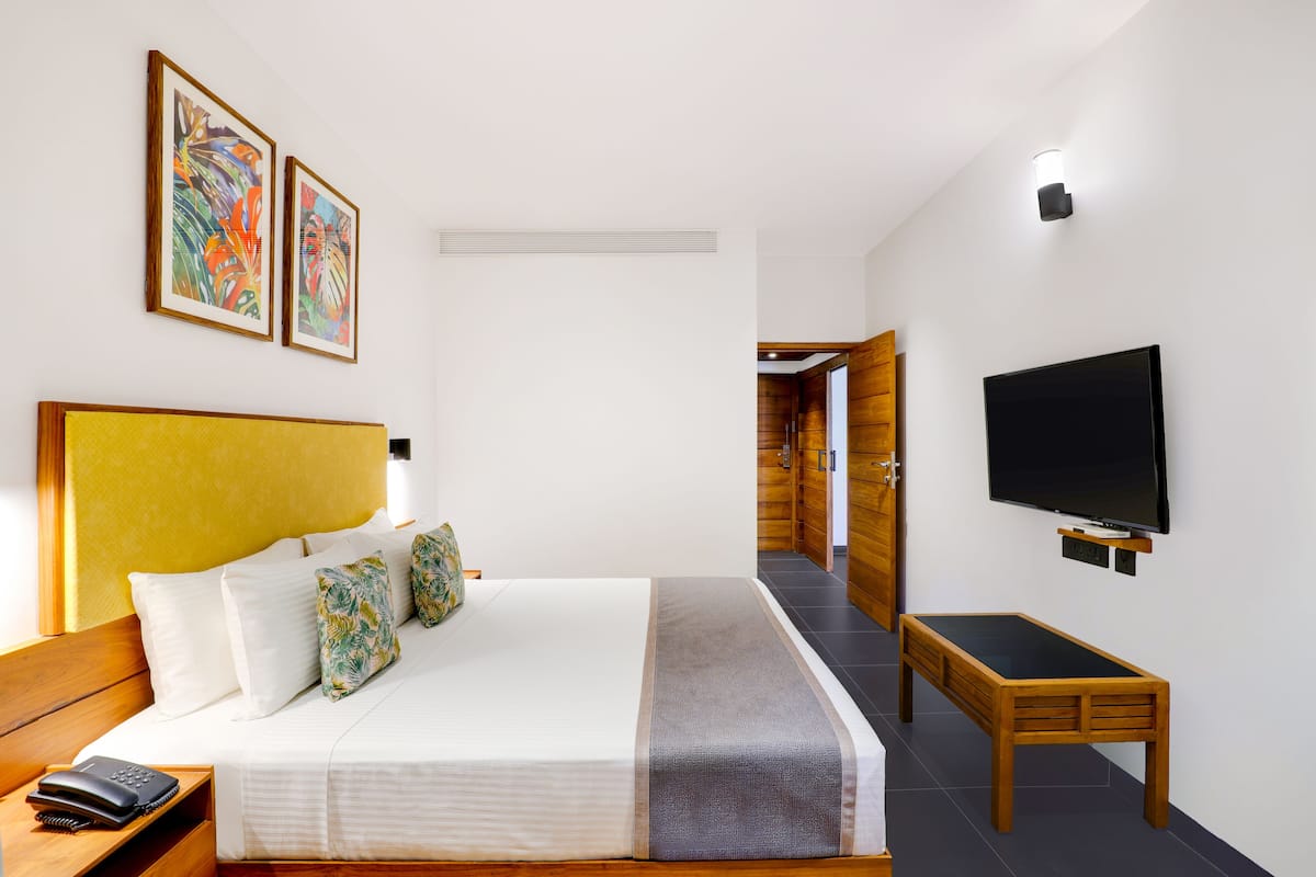 Habitación de hotel con cama, mesita de noche con teléfono, televisor y una obra de arte en la pared.