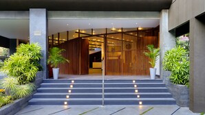 A modern hotel entrance with a staircase leading to the lobby, surrounded by potted plants and a wooden partition.