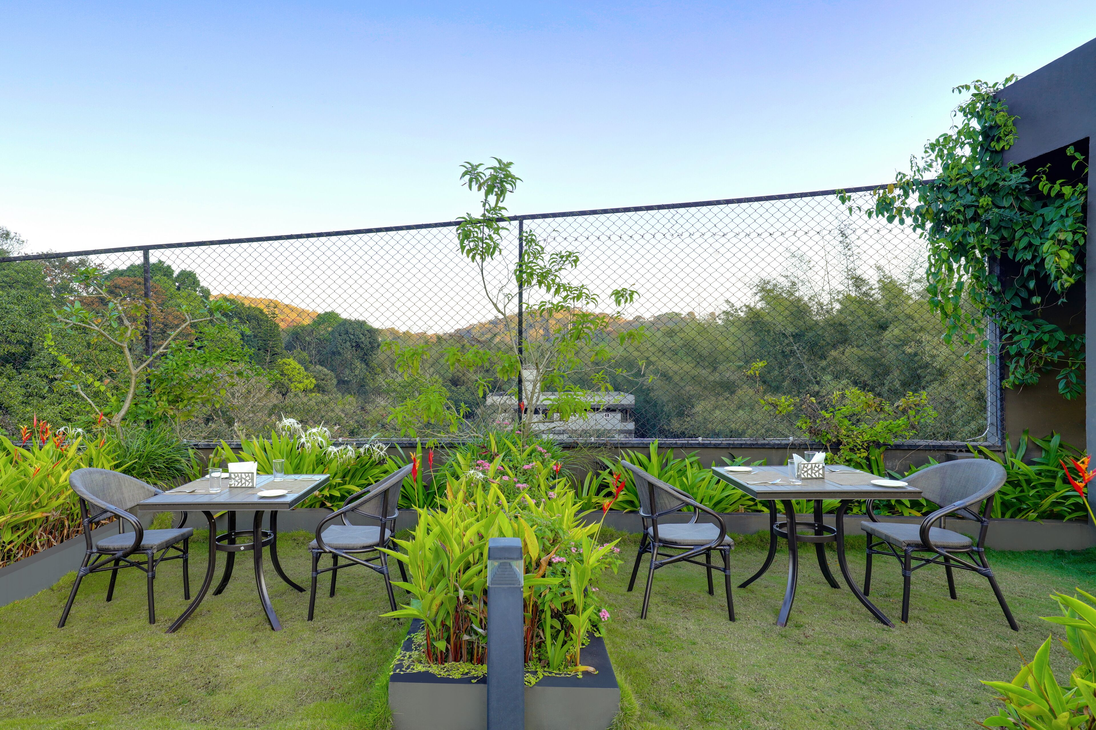 An outdoor patio with a table and chairs, surrounded by lush greenery and a view of hills.
