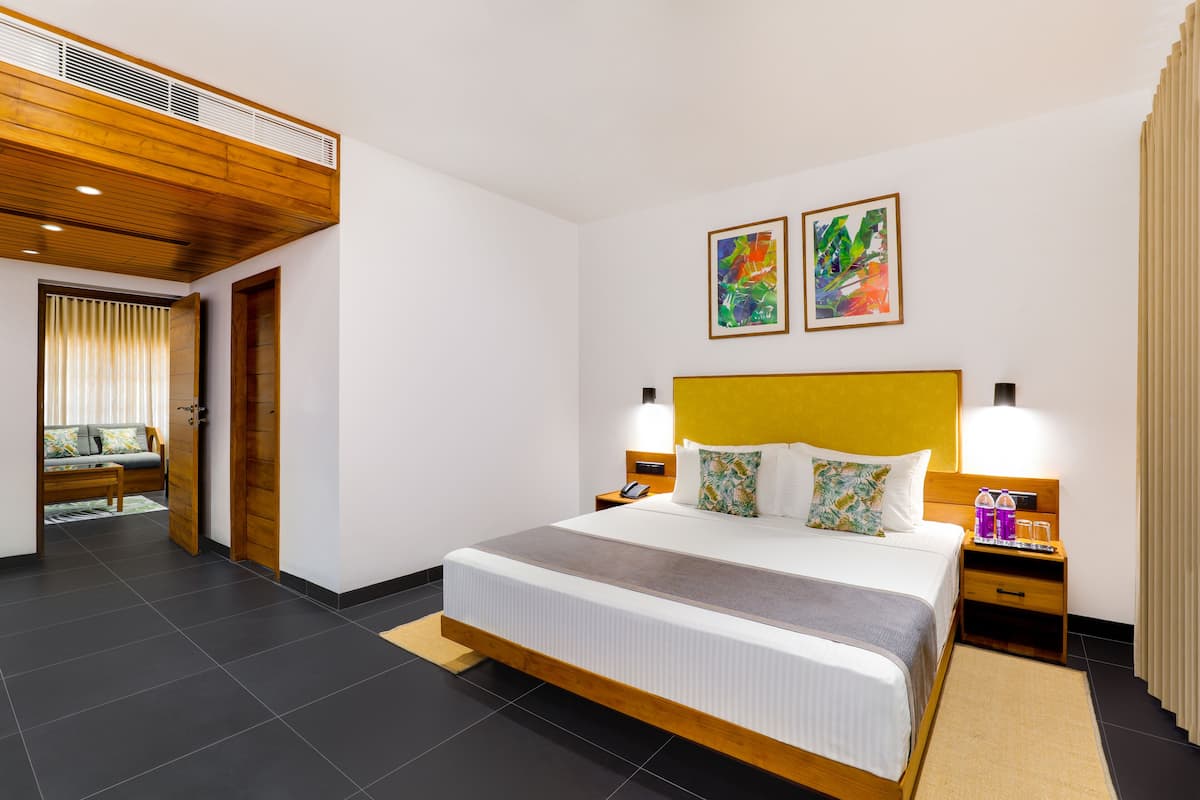 Una habitación de hotel moderna con una cama grande, cabecera de madera, dos mesitas de noche con lámparas y obras de arte en las paredes.
