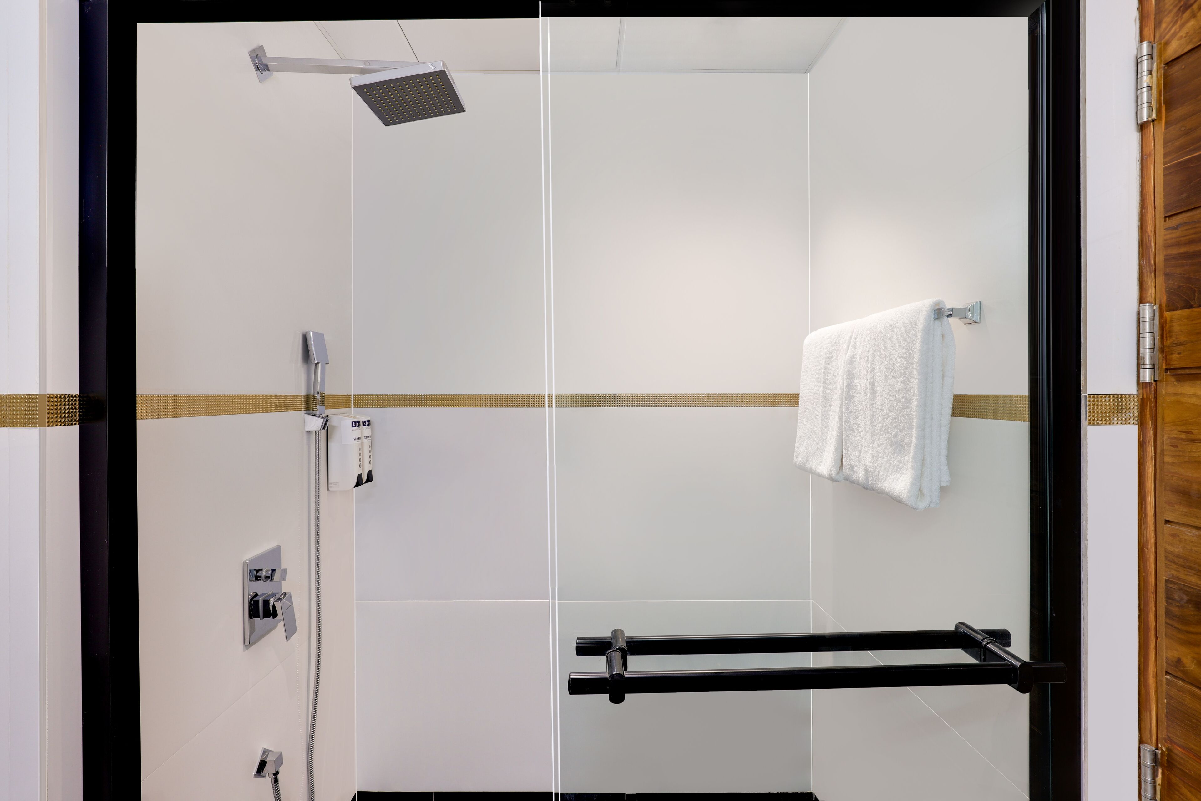 A modern bathroom with a glass shower enclosure, a towel rack, and a visible electrical outlet.