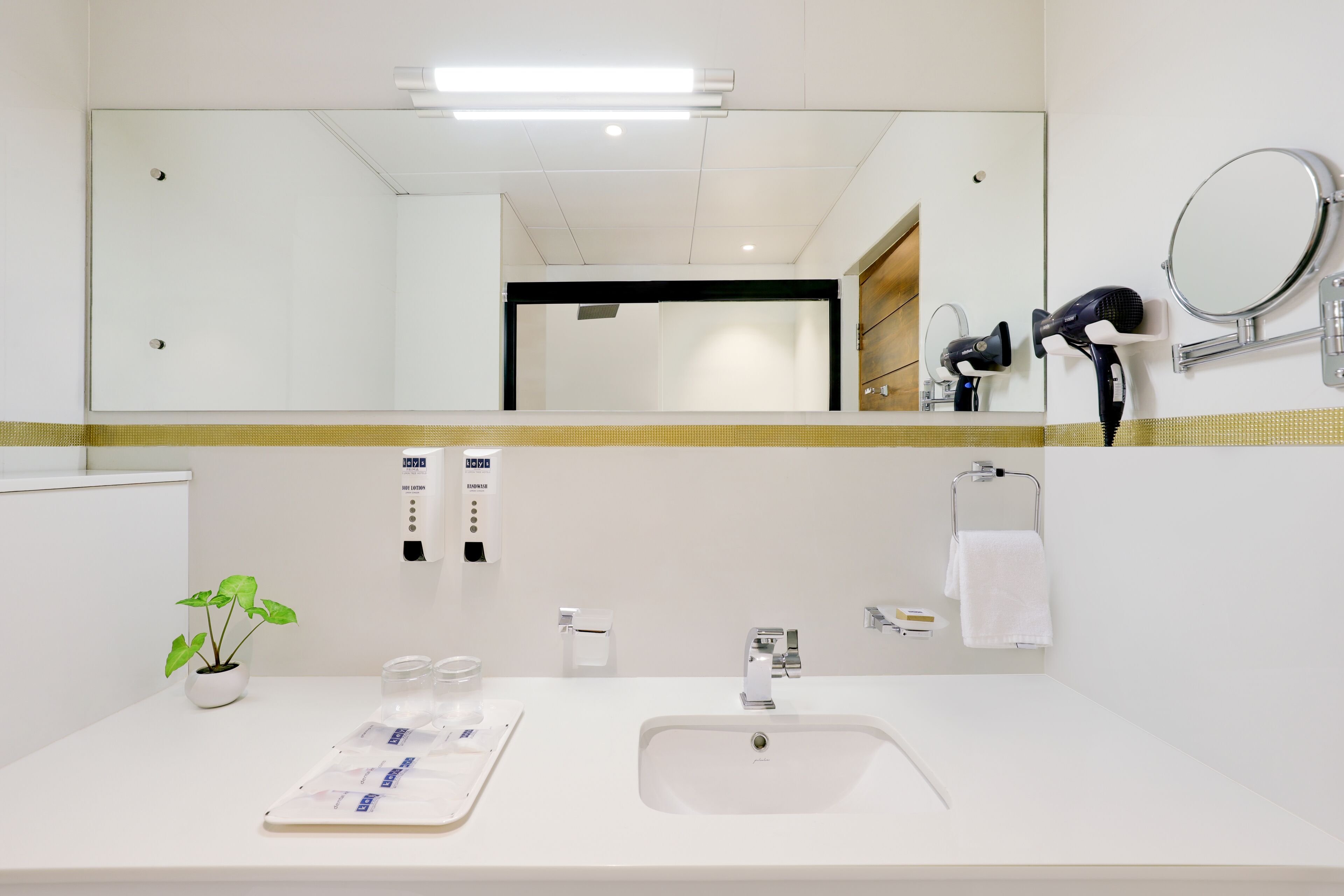 Baño de hotel con un espejo grande, un lavabo, un secador de pelo y un perchero para toallas.