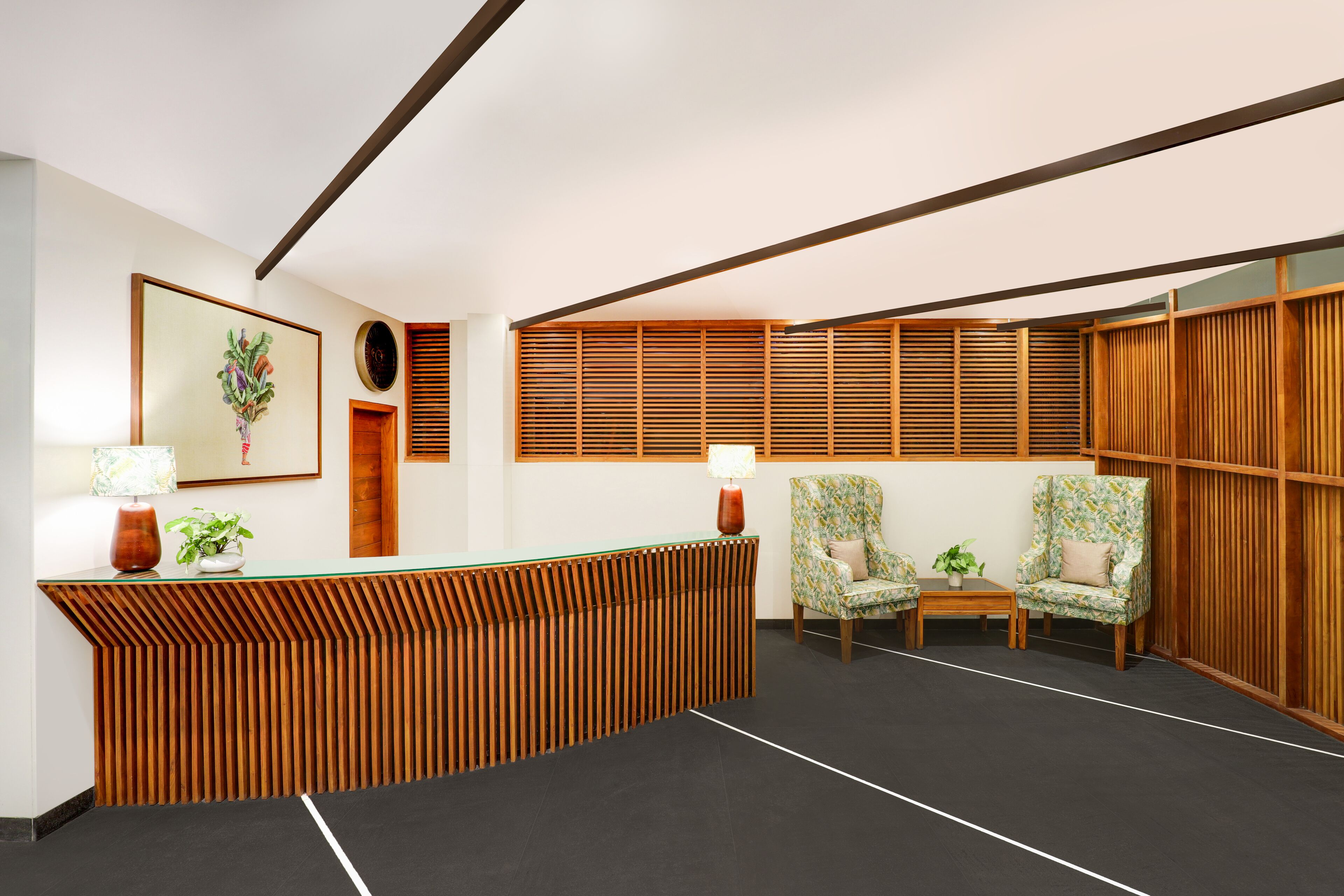 A reception area with a wooden reception desk, two patterned armchairs, a small table, and a wall-mounted painting.