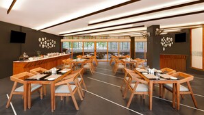 A modern dining area with wooden tables and chairs, a long counter with a barista station, and large windows offering a view of the outdoors.