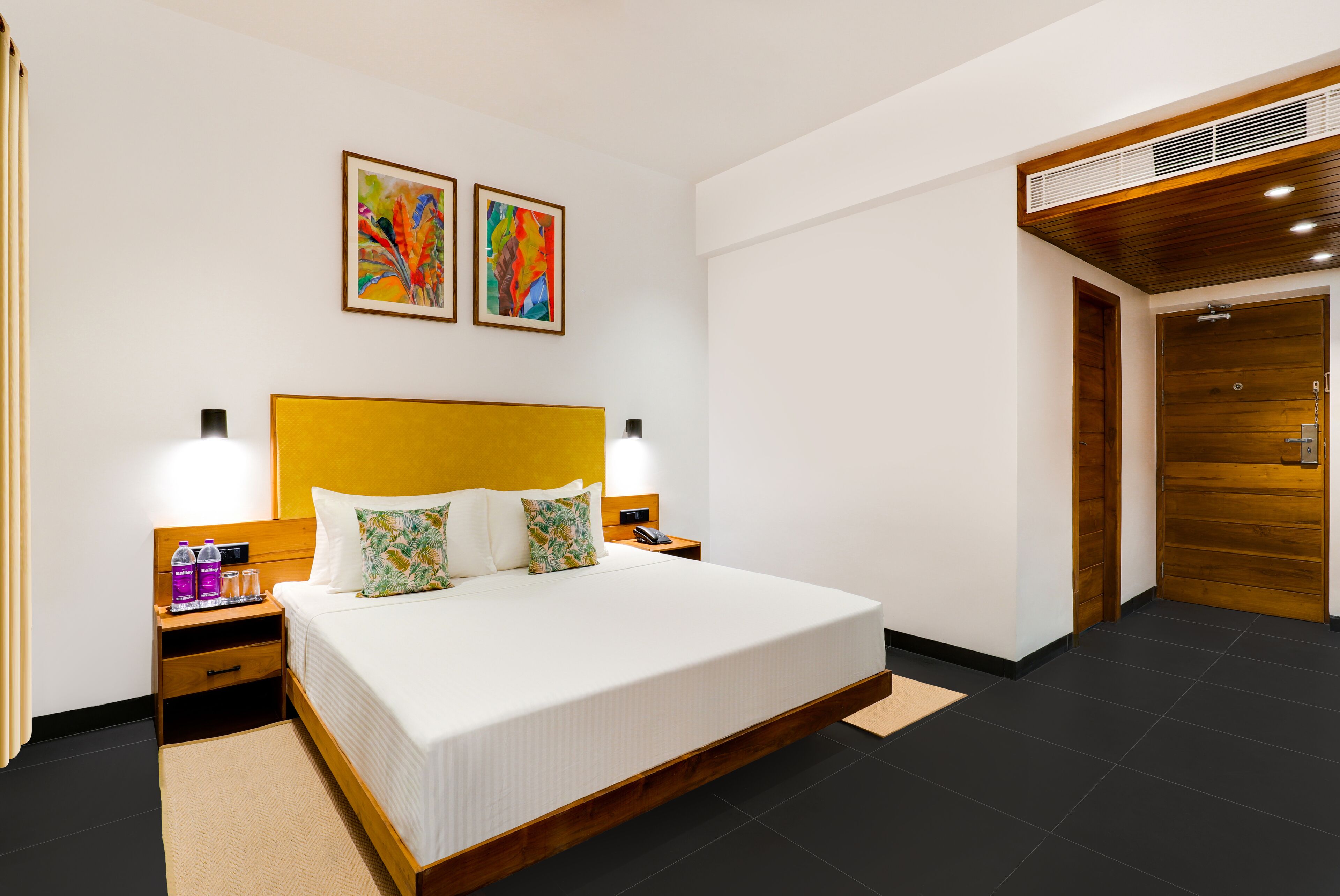 A modern hotel room with a large bed, wooden headboard, two bedside tables with lamps, and artwork on the wall.
